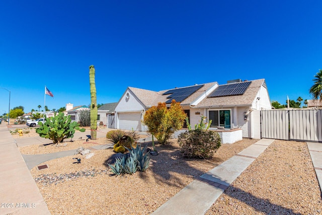 ranch-style home featuring roof mounted solar panels, a shingled roof, fence, and a gate