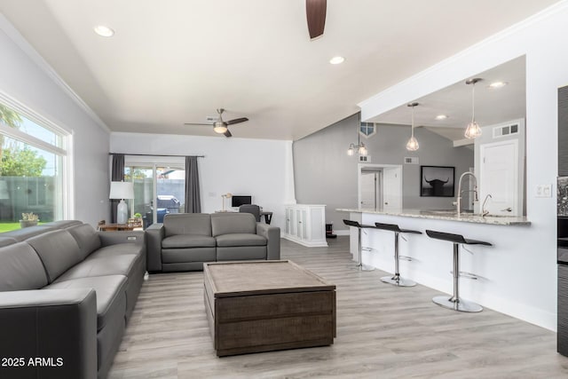 living area with a ceiling fan, vaulted ceiling, light wood-style floors, ornamental molding, and recessed lighting