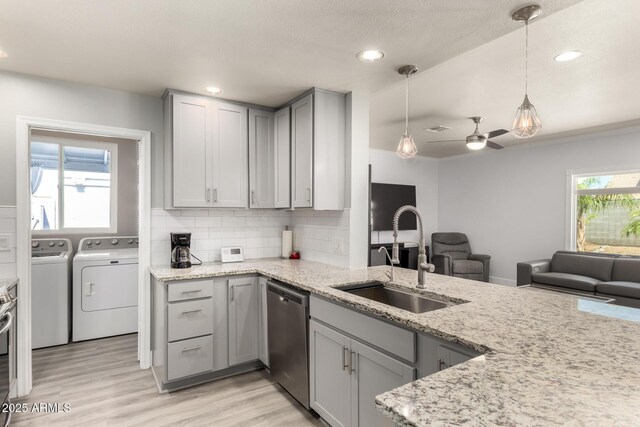 kitchen with stainless steel dishwasher, washing machine and clothes dryer, a sink, gray cabinetry, and light stone counters
