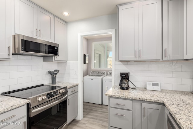 kitchen featuring appliances with stainless steel finishes, independent washer and dryer, tasteful backsplash, and light wood-type flooring
