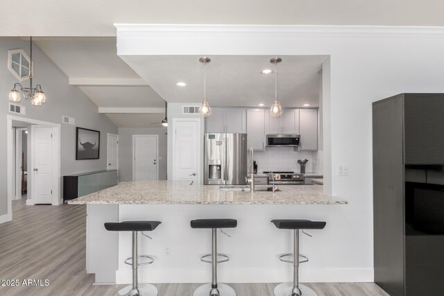kitchen with appliances with stainless steel finishes, decorative backsplash, a breakfast bar, lofted ceiling, and light wood finished floors