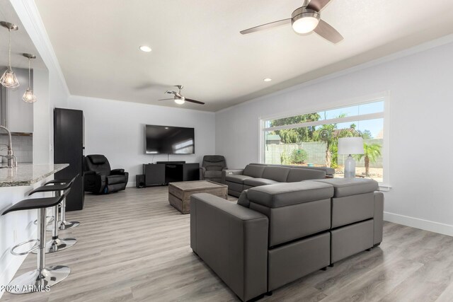 living room featuring a ceiling fan, crown molding, light wood-style floors, baseboards, and recessed lighting