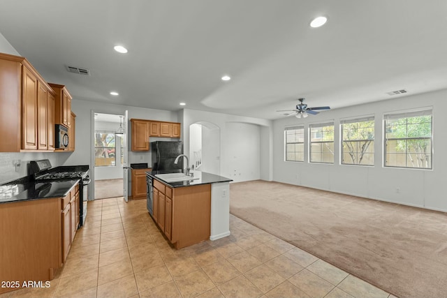 kitchen featuring an island with sink, ceiling fan, light colored carpet, black appliances, and sink