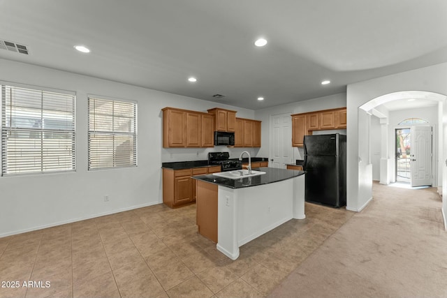 kitchen with black appliances, light tile patterned floors, sink, and an island with sink