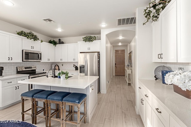 kitchen with white cabinets, a kitchen bar, stainless steel appliances, and an island with sink