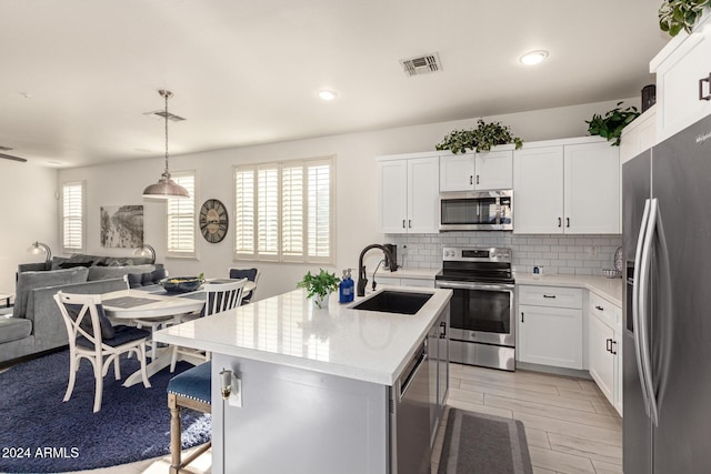 kitchen with a kitchen island with sink, hanging light fixtures, sink, appliances with stainless steel finishes, and white cabinetry