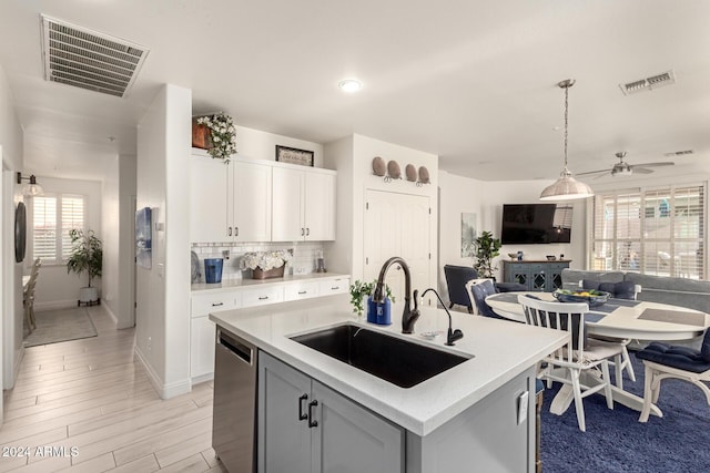 kitchen featuring sink, stainless steel dishwasher, an island with sink, white cabinets, and light wood-type flooring