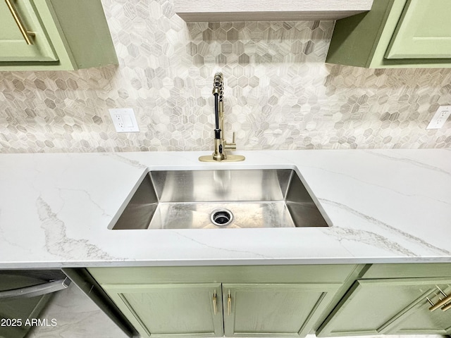 interior details with green cabinetry, light stone counters, decorative backsplash, and a sink