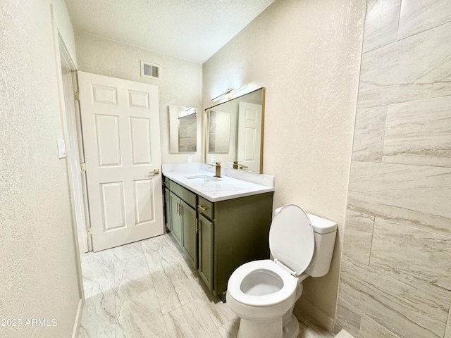 bathroom featuring toilet, marble finish floor, vanity, visible vents, and a textured wall