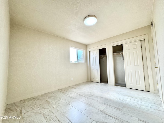 unfurnished bedroom with baseboards, marble finish floor, two closets, and a textured ceiling