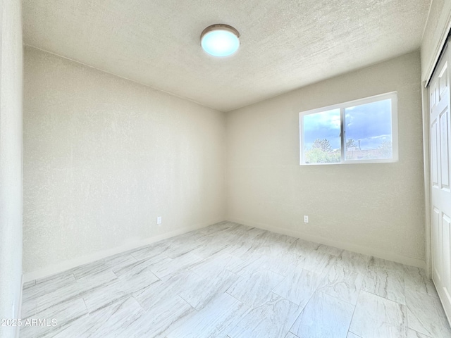 spare room featuring a textured ceiling and baseboards
