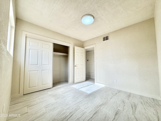 unfurnished bedroom with a closet, a textured ceiling, baseboards, visible vents, and a textured wall