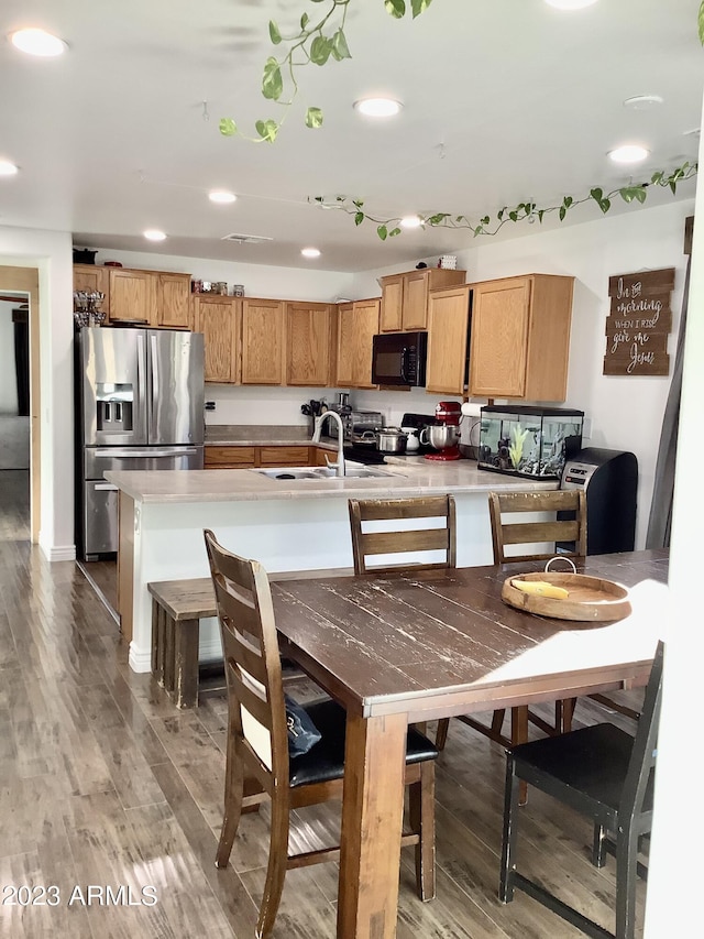 kitchen with dark hardwood / wood-style floors, a kitchen island with sink, sink, a kitchen bar, and appliances with stainless steel finishes