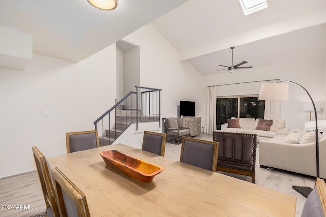 dining space with ceiling fan, vaulted ceiling with skylight, and light hardwood / wood-style flooring