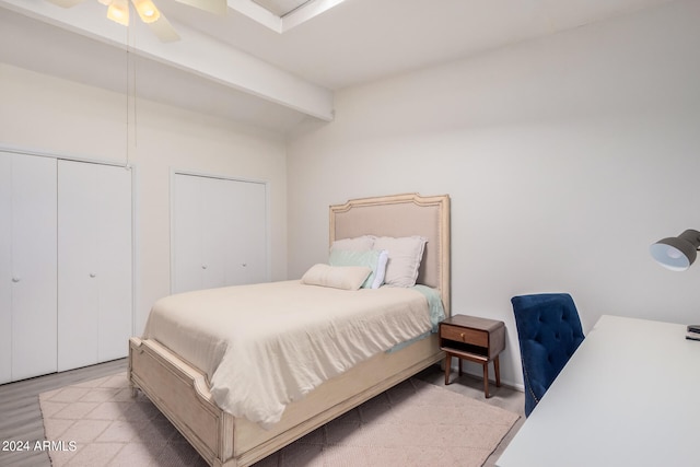 bedroom with beam ceiling, light hardwood / wood-style floors, ceiling fan, and multiple closets