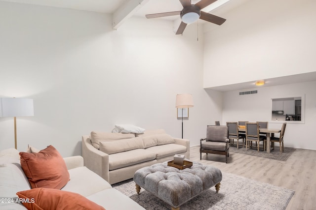 living room with light wood-type flooring, beam ceiling, a towering ceiling, and ceiling fan