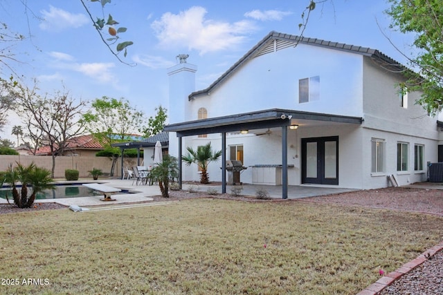 rear view of house with fence, stucco siding, french doors, a yard, and a patio