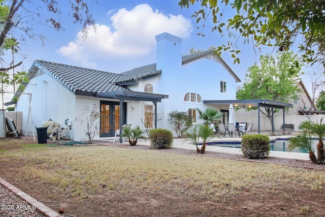 rear view of property with a patio, a fenced in pool, stucco siding, french doors, and a tile roof
