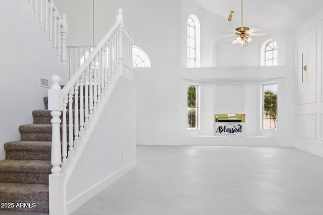 stairs featuring plenty of natural light, ceiling fan with notable chandelier, baseboards, and a towering ceiling