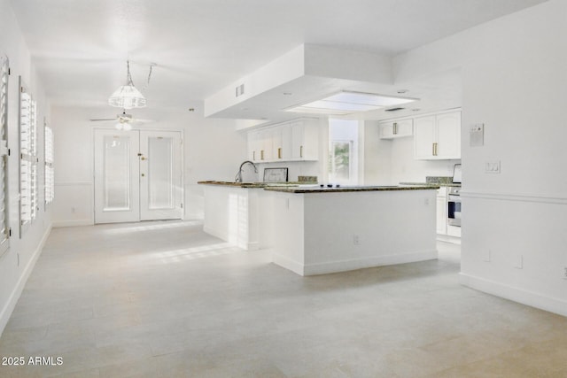 kitchen with dark countertops, oven, baseboards, white cabinetry, and a sink
