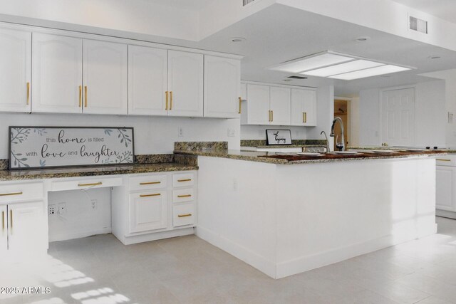 kitchen featuring visible vents, white cabinets, a peninsula, and dark stone countertops
