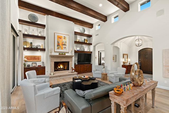 living room featuring light wood-type flooring, a high ceiling, beamed ceiling, and a notable chandelier