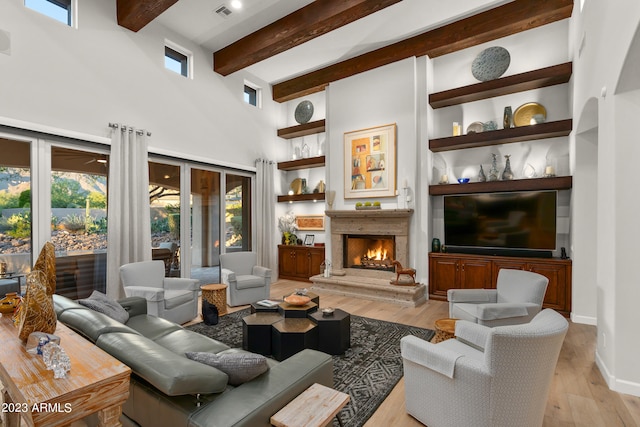 living room featuring beam ceiling, a towering ceiling, light hardwood / wood-style flooring, and built in features