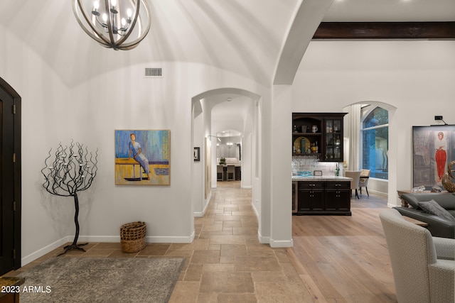 hallway with an inviting chandelier, a towering ceiling, beam ceiling, and light hardwood / wood-style floors