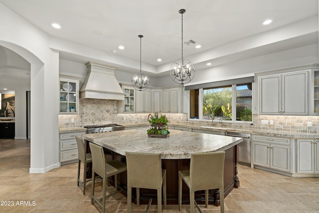 kitchen featuring appliances with stainless steel finishes, decorative backsplash, a center island, premium range hood, and a notable chandelier