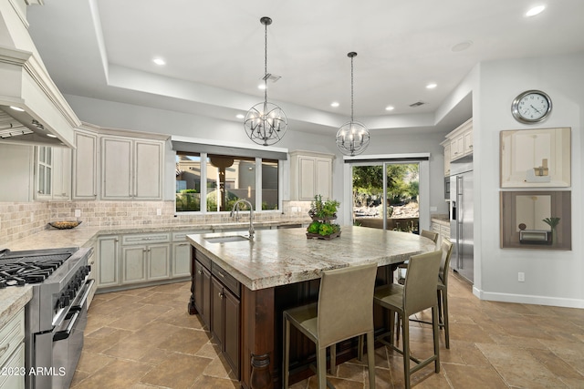 kitchen with sink, an island with sink, high end appliances, a notable chandelier, and cream cabinets