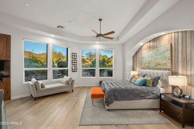 bedroom with a tray ceiling, light hardwood / wood-style floors, and ceiling fan