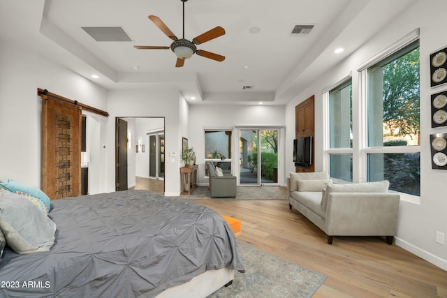 bedroom featuring light hardwood / wood-style flooring, a tray ceiling, ceiling fan, and a barn door