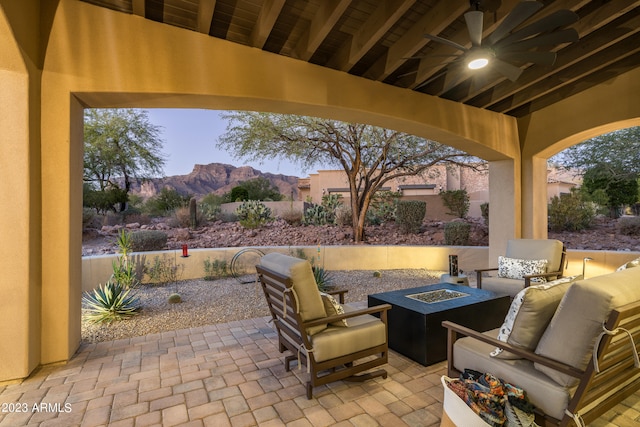 patio terrace at dusk with ceiling fan, a mountain view, and an outdoor living space with a fire pit