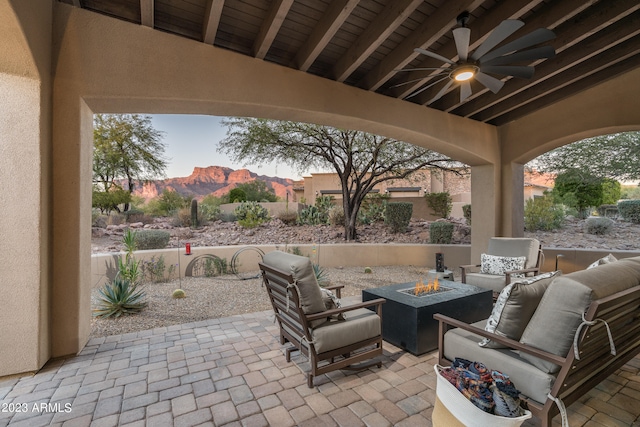 patio terrace at dusk featuring a mountain view, ceiling fan, and an outdoor living space with a fire pit