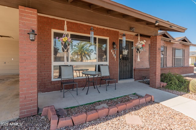 doorway to property featuring visible vents, a porch, and brick siding