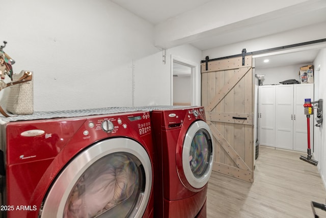 clothes washing area with laundry area, a barn door, independent washer and dryer, and wood finished floors