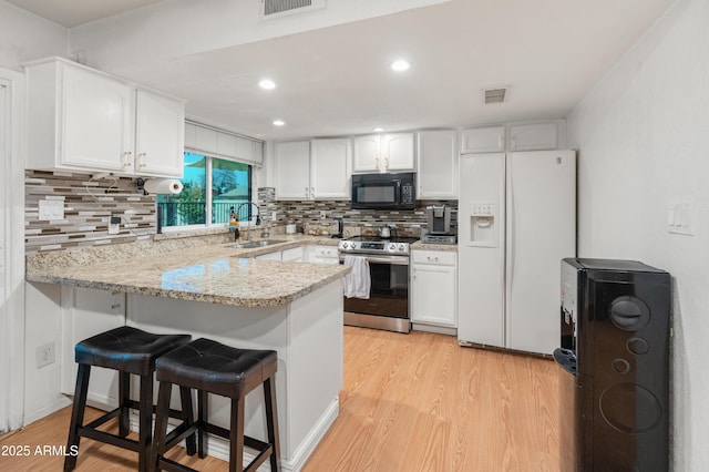 kitchen with electric range, white refrigerator with ice dispenser, visible vents, a peninsula, and black microwave