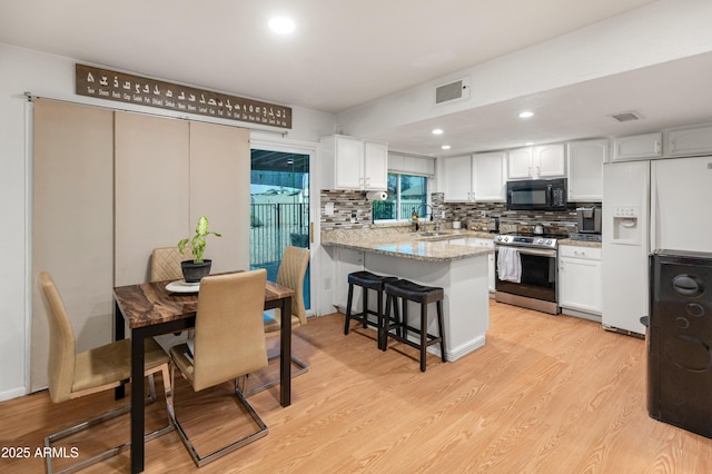 kitchen with black microwave, a peninsula, stainless steel range with electric cooktop, white fridge with ice dispenser, and light wood finished floors