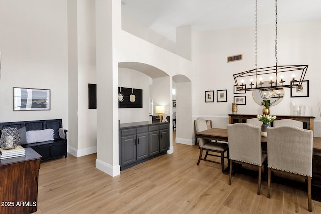 9821 E Windrose Dr, Scottsdale, AZ 85260 - dining area featuring arched walkways, light wood-style flooring, a high ceiling, and a chandelier