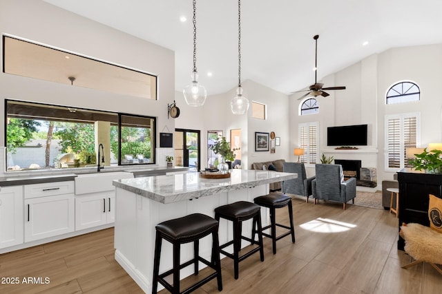 9821 E Windrose Dr, Scottsdale, AZ 85260 - kitchen featuring high vaulted ceiling, a center island, white cabinetry, light stone counters, and light wood finished floors