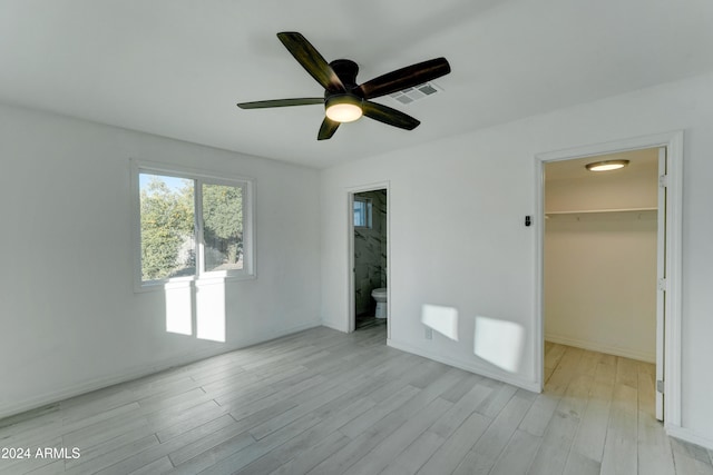 unfurnished bedroom featuring a walk in closet, ceiling fan, light wood-type flooring, connected bathroom, and a closet