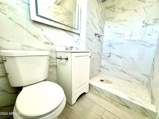 bathroom featuring vanity, hardwood / wood-style flooring, toilet, tiled shower, and tile walls