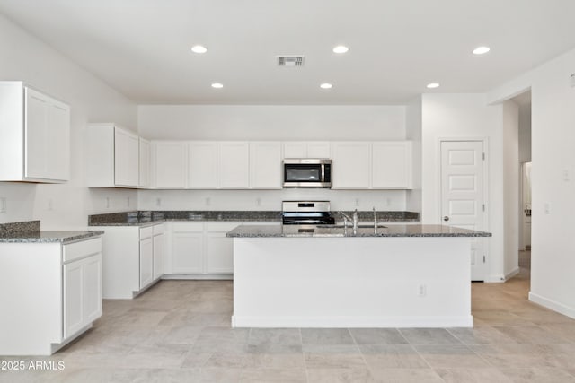 kitchen with white cabinetry, an island with sink, dark stone countertops, and appliances with stainless steel finishes