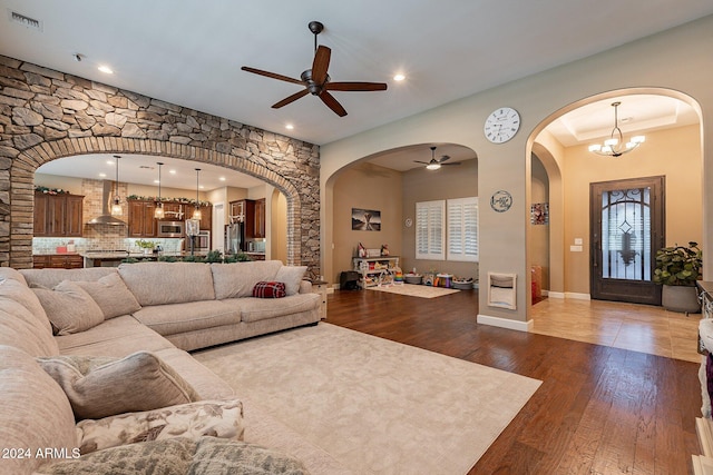 living room with ceiling fan with notable chandelier and dark hardwood / wood-style floors