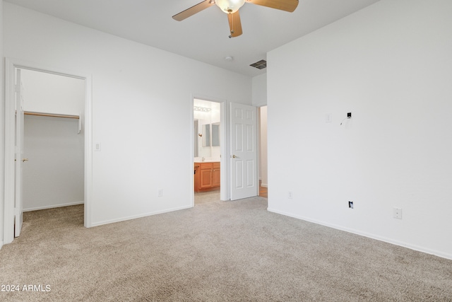 unfurnished bedroom featuring a walk in closet, light carpet, and ensuite bath