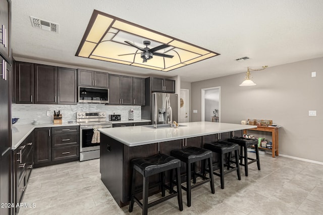 kitchen featuring decorative backsplash, an island with sink, stainless steel appliances, a kitchen bar, and ceiling fan