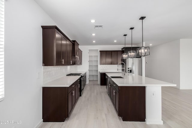 kitchen featuring dark brown cabinetry, sink, decorative light fixtures, a center island with sink, and appliances with stainless steel finishes