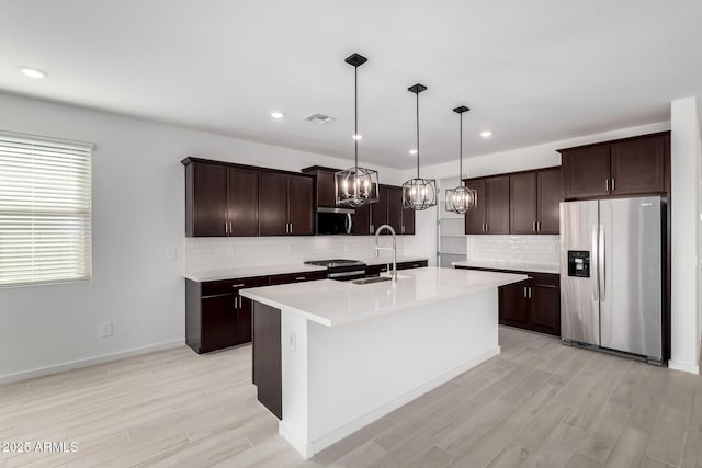 kitchen with sink, decorative light fixtures, dark brown cabinets, a center island with sink, and stainless steel appliances