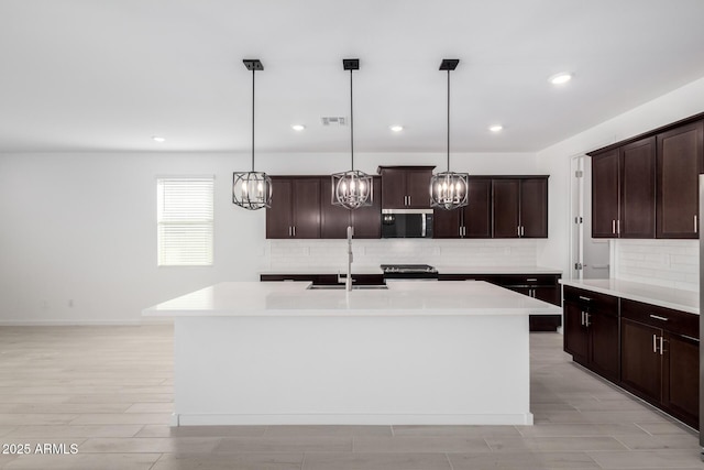 kitchen with an island with sink, sink, pendant lighting, and dark brown cabinetry