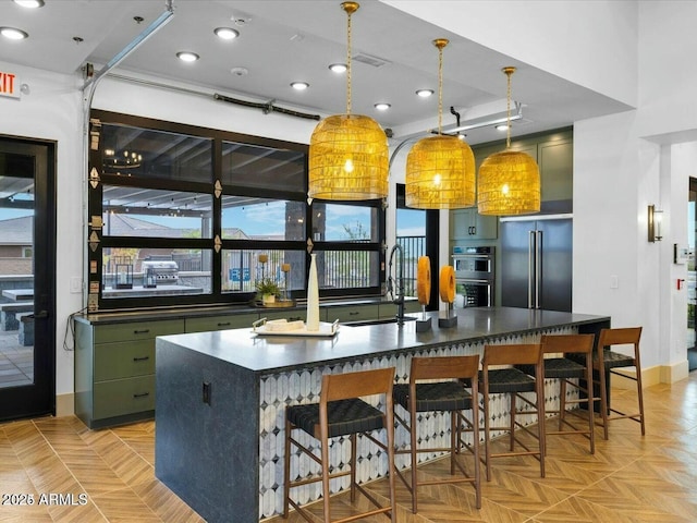 kitchen with a breakfast bar, sink, high end refrigerator, hanging light fixtures, and a center island with sink